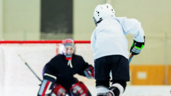 Hockey player in white jersey approaches goalie on ice rink.