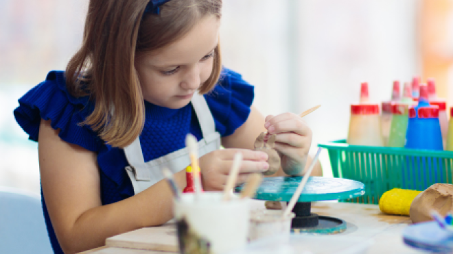 Child painting at a table, surrounded by colorful art supplies.