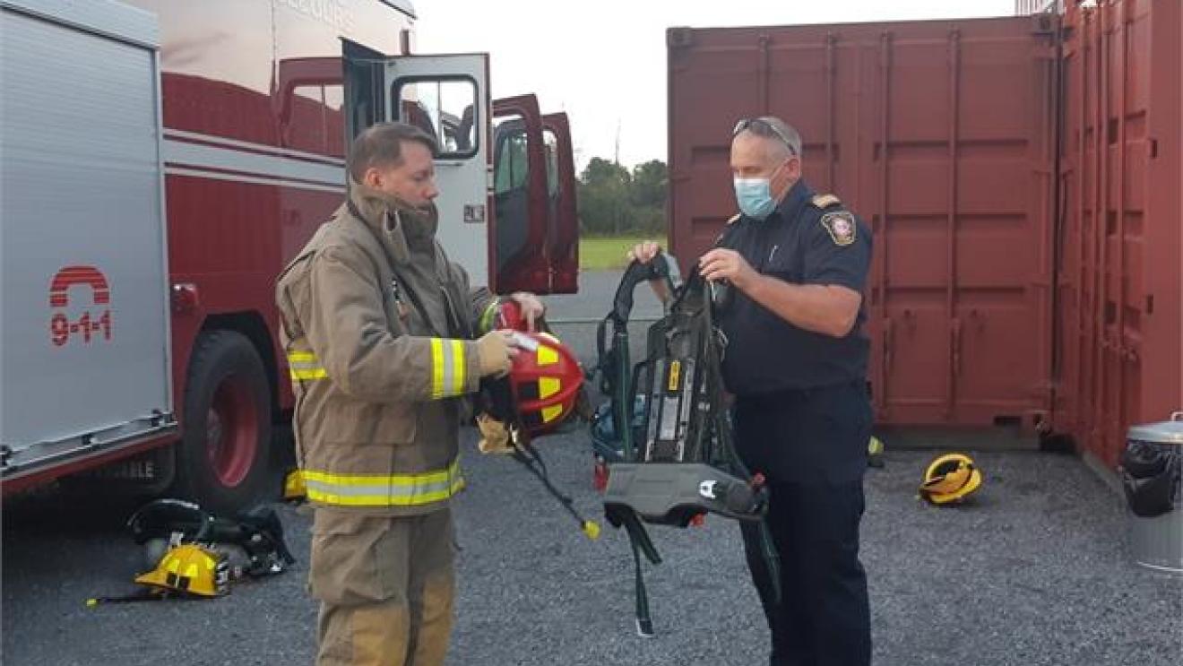 Firefighters in gear, standing next to a fire truck, exchanging equipment.