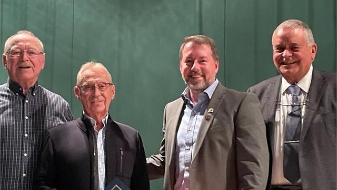 Four men standing together, two wearing suits, in front of a green curtain.