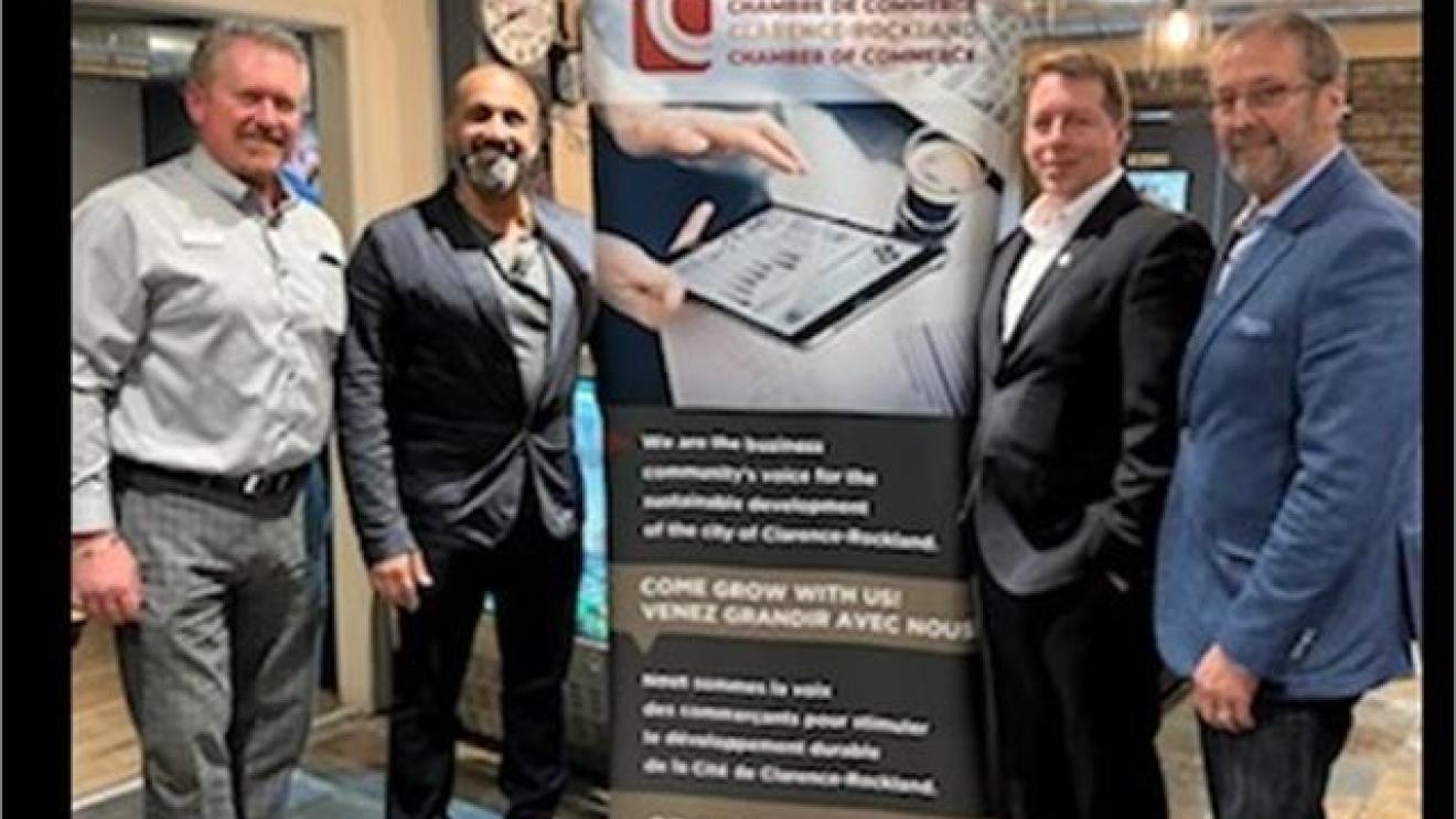 Four men standing beside a Chamber of Commerce banner in an office setting.