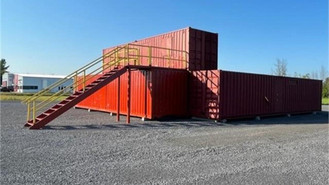Red shipping containers stacked with stairs on gravel under a clear blue sky.