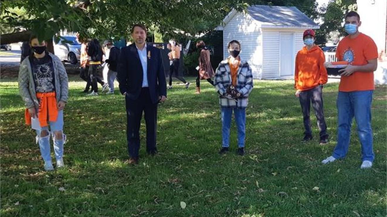 Group of people wearing masks standing on grass outside.