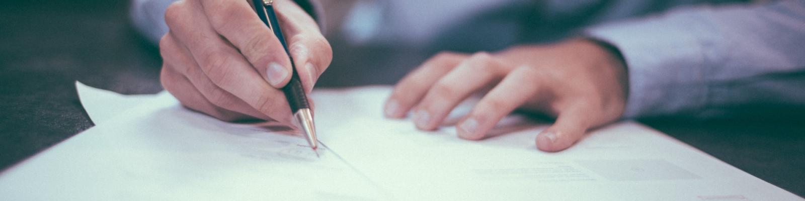 Hand writing with a pen on paper, office setting.