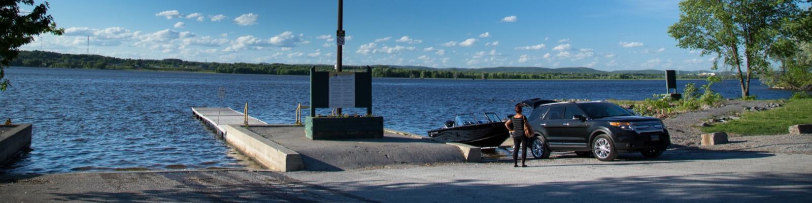 A car parked by a lakeside dock under a blue sky with scattered clouds.