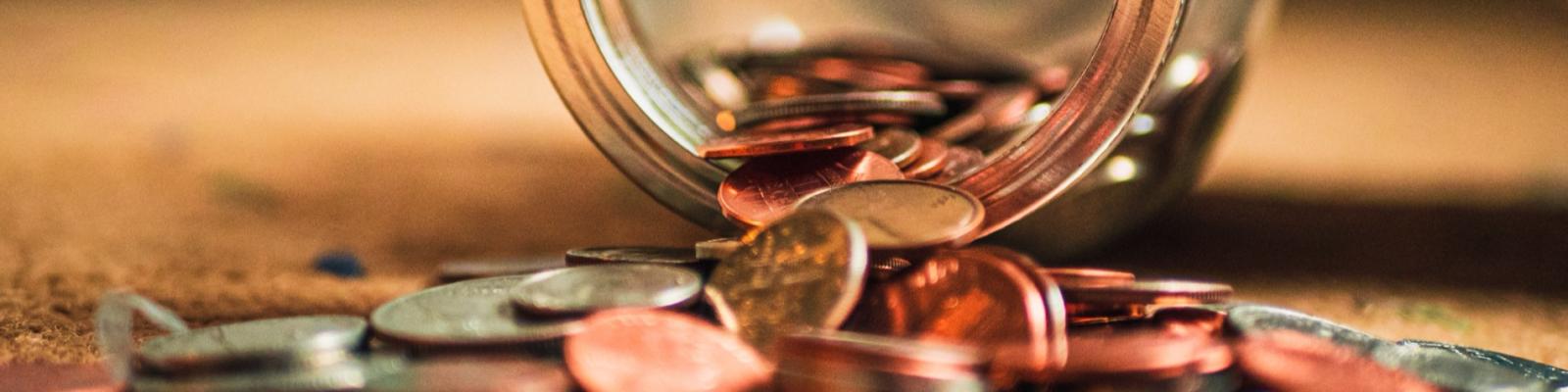 Coins spilling from overturned jar onto wooden surface.