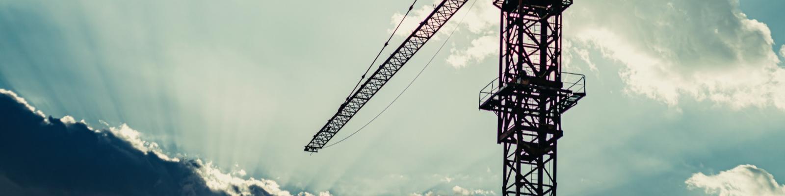 Construction crane against a cloudy sky, sun rays peeking through.